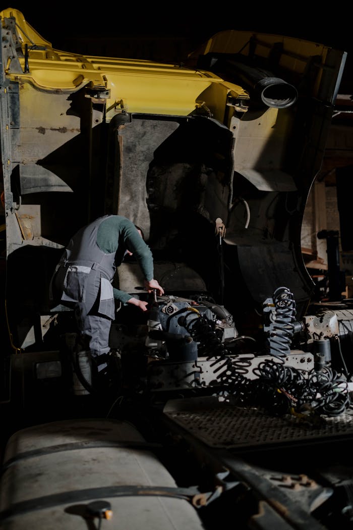 Mechanic working on a truck engine repair at night in a dimly lit garage.