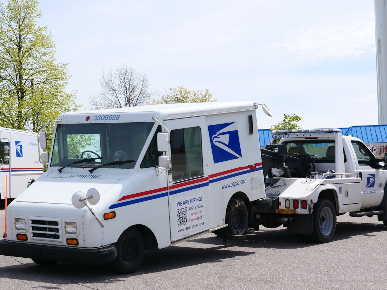 A United States Postal Service (USPS) mail truck is being towed outdoors on a clear day.